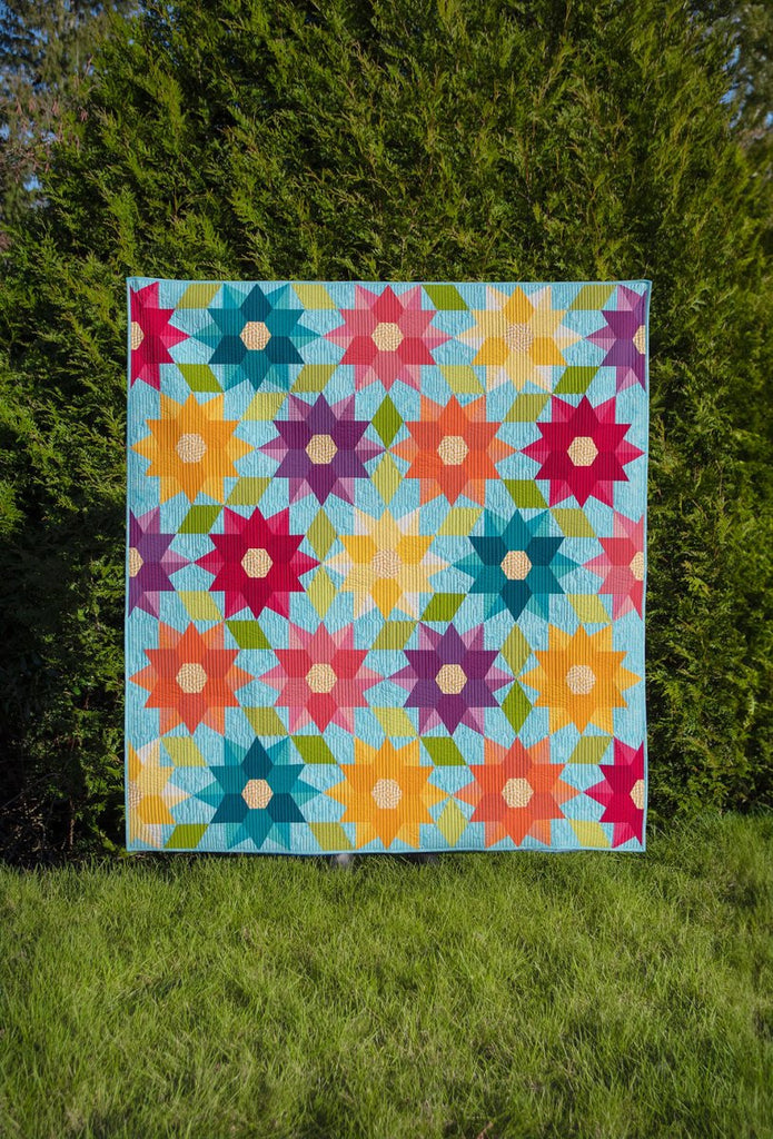 Dancing Dahlias Paper Quilt Pattern by Krista Moser | The Quilted Life - Entire quilt displayed outdoors with a green arborvitae tree behind it